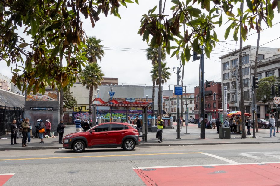 Street scene featuring a red car, people walking, a mural, palm trees, and a colorful storefront in an urban environment.