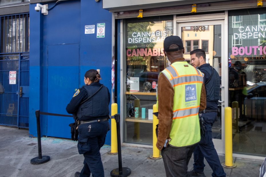 People, including two police officers and a person in a safety vest, stand outside a cannabis dispensary.