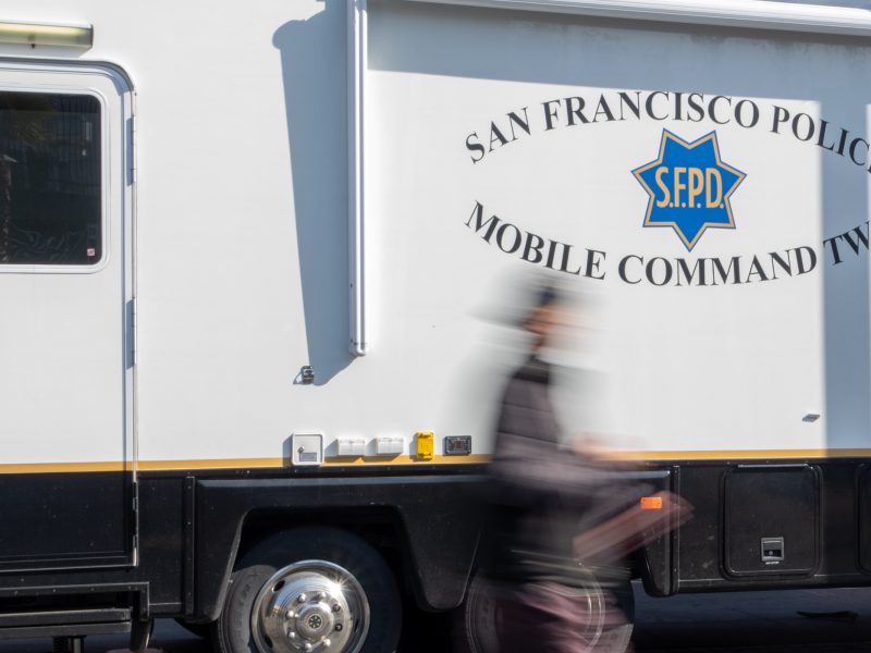 A person walks by a parked San Francisco Police Mobile Command vehicle with the logo and "Mobile Command Two" text visible.