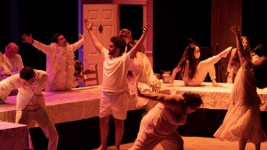 A group of performers in white costumes strike dramatic poses on stage with expressions of intensity and movement.