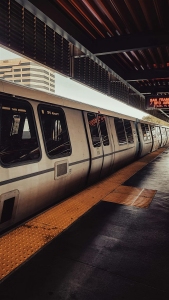 A train is stopped at an outdoor station platform under a canopy, with buildings visible in the background.