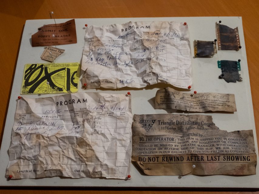 A display board with old movie tickets, handwritten program notes, labels, and small film negatives pinned to it.