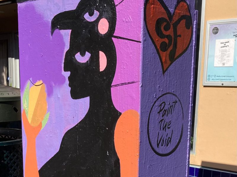 A painted utility box features a black silhouette of a person holding a yellow fruit, with abstract shapes and a heart labeled "SF" on a purple background.
