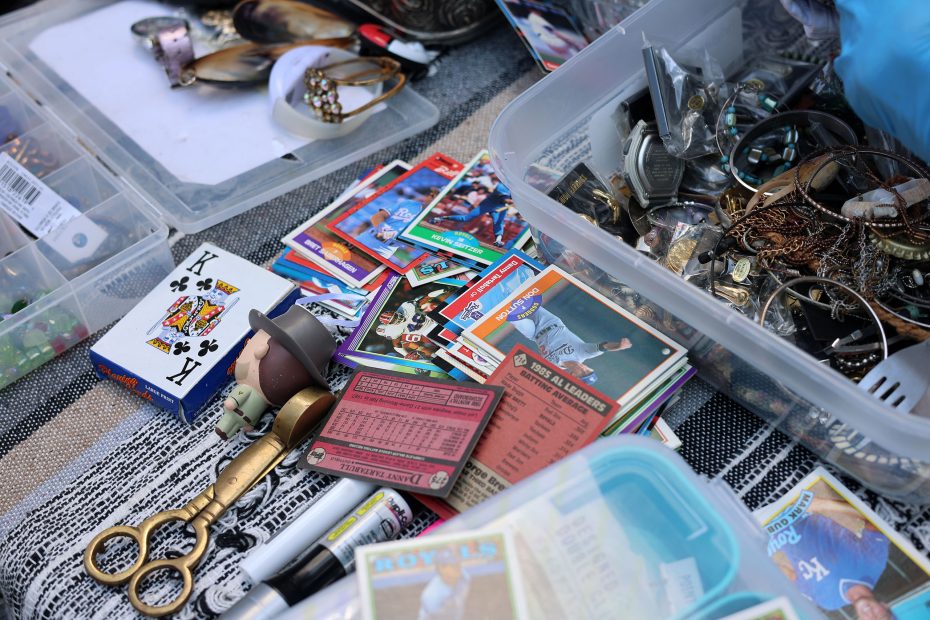 Assorted sports trading cards, jewelry, and small items are spread out on a table, including a deck of cards, keys, and plastic containers.