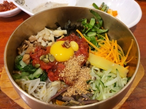 A bowl of bibimbap with assorted vegetables, a raw egg yolk, red chili paste, sesame seeds, and pumpkin seeds, served on rice.