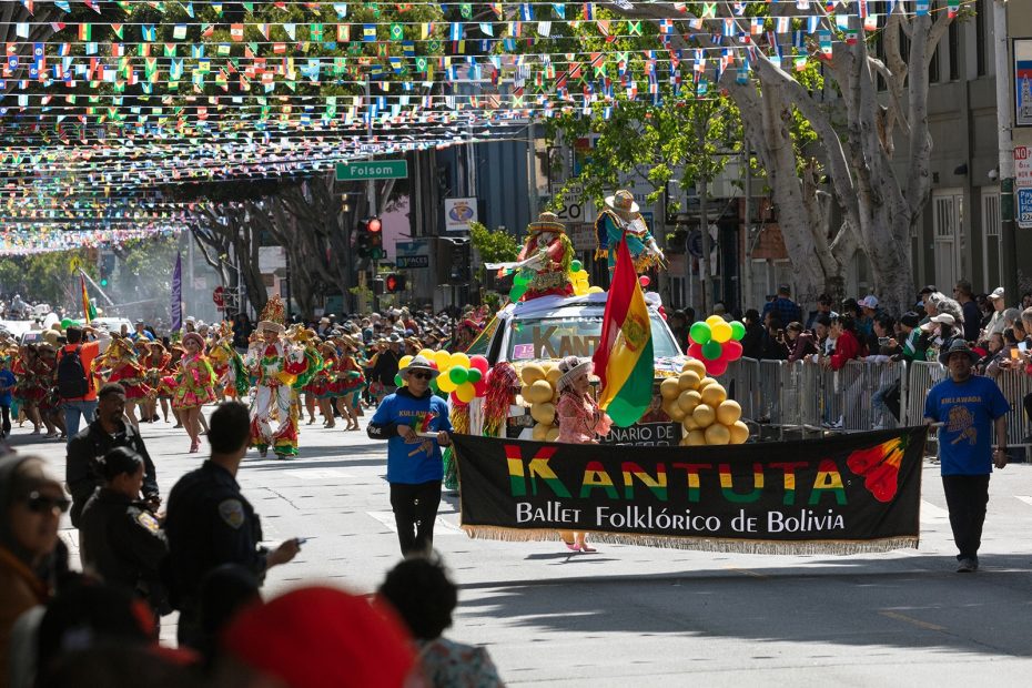 A parade features people holding a "Kantuta Ballet Folklórico de Bolivia" banner, colorful costumes, balloons, and Bolivian flags, with spectators and festive decorations overhead.