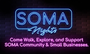 Neon sign reads "SOMA Nights" with text below: "Come Walk, Explore, and Support SOMA Community & Small Businesses" against a dark brick wall background.