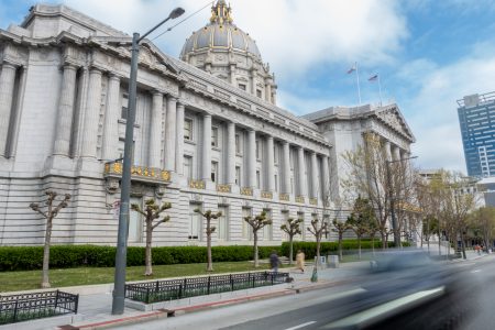 A grand government building with columns and a large dome, seen from the street with blurred motion of a passing car in the foreground.