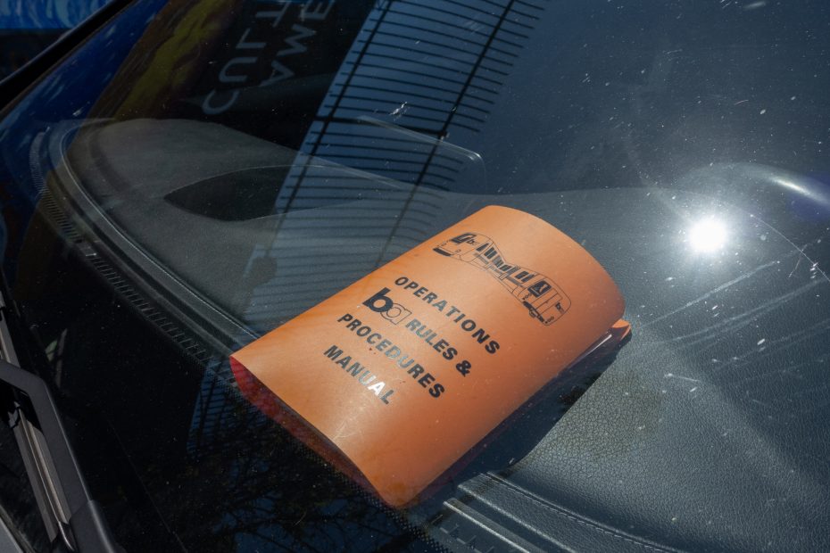 An orange "Operations Policies & Procedures Manual" booklet is placed on the windshield of a vehicle in sunlight.