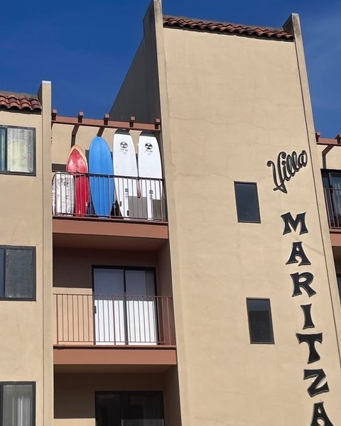 Four surfboards in different colors are standing upright on the balcony of an apartment building labeled "Villa Maritza.