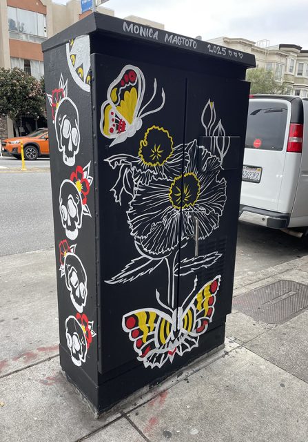 A utility box on a city sidewalk painted with a large white and yellow flower, butterflies, and stylized skulls on a black background.