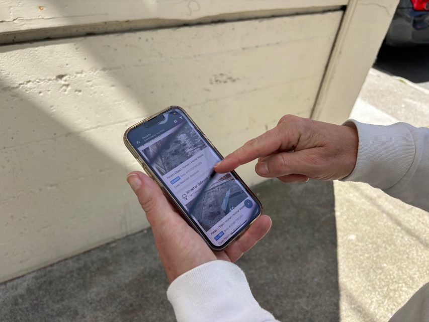 A person uses a smartphone app with a map and location-based notifications while standing outside near a concrete wall.