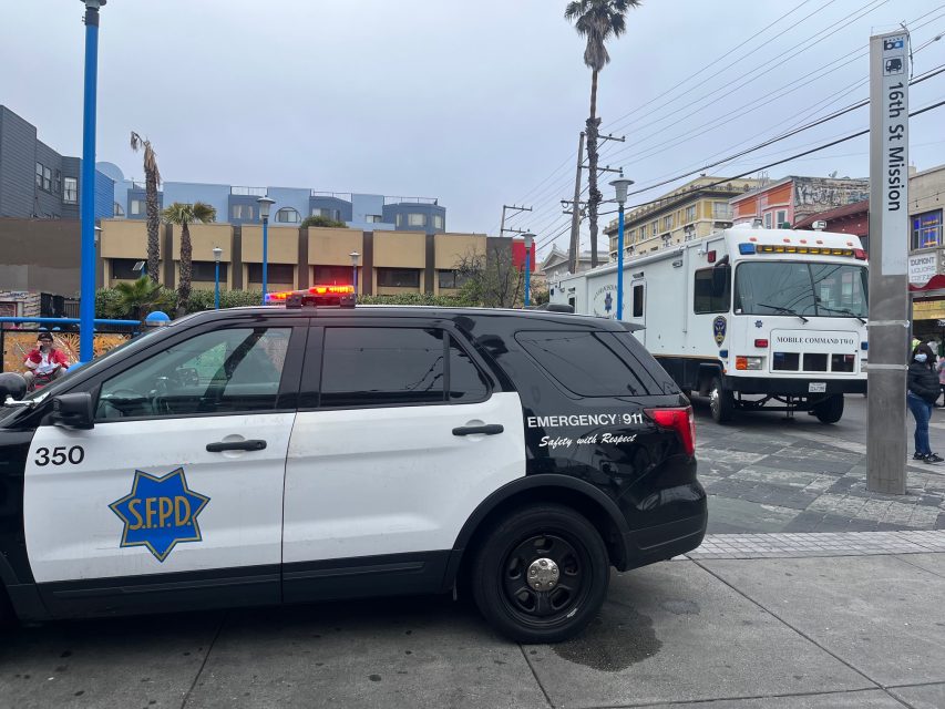 A San Francisco police SUV and mobile command vehicle are parked at 16th St Mission station; lights are flashing and officers are present.