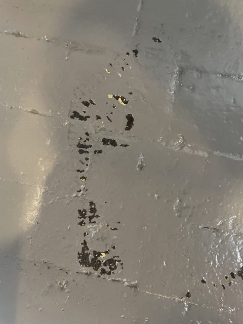 A gray painted brick wall with some areas where the paint has chipped away, revealing patches of the underlying surface.