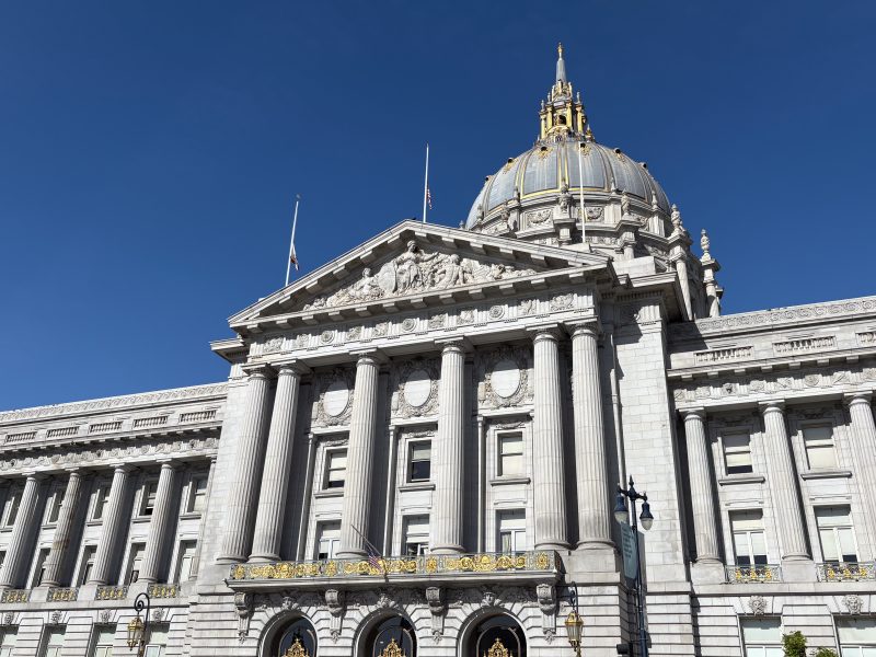 A neoclassical building with tall columns, ornate carvings, and a large dome topped with a gilded structure against a clear blue sky.