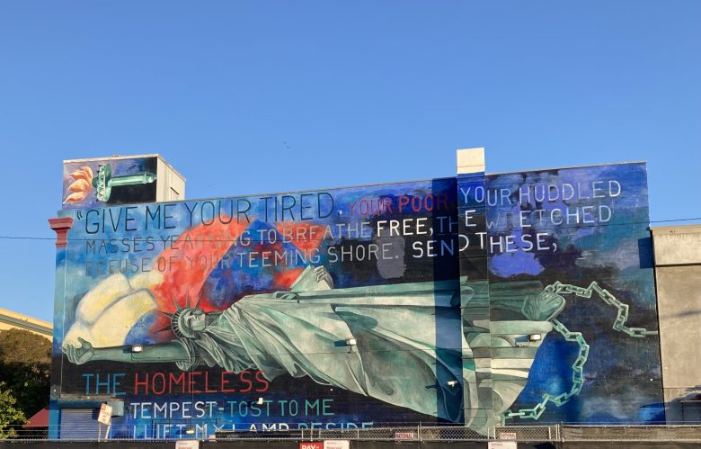 A mural on a building depicts the Statue of Liberty with broken chains and features an excerpt from Emma Lazarus’s poem about welcoming the poor and homeless.