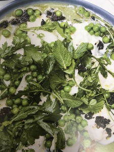 Fresh green peas and mixed herbs, including mint and parsley, are arranged on a creamy white sauce in a blue-rimmed dish.