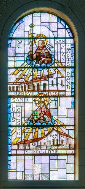 Stained glass window depicting San Juan Capistrano and San Luis Obispo missions with portraits of saints, mission buildings, and dates of their founding.