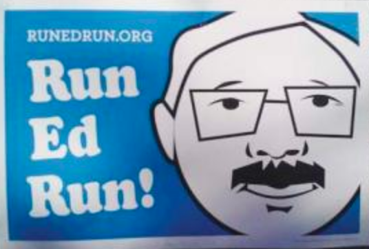 A blue and white sign displays the text "Run Ed Run!" alongside a stylized illustration of a man's face with glasses and a mustache. The website "RUNEDRUN.ORG" is at the top left.
