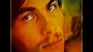 Close-up of a young man with a mustache looking directly at the camera; the image has a warm, yellowish tint.