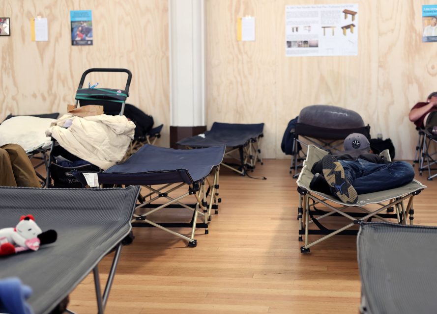 Several cots with bedding and personal items are arranged in a room with wood-paneled walls; a person is lying on one cot.