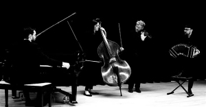 Four musicians perform on stage with a piano, double bass, violin, and bandoneon against a dark background.