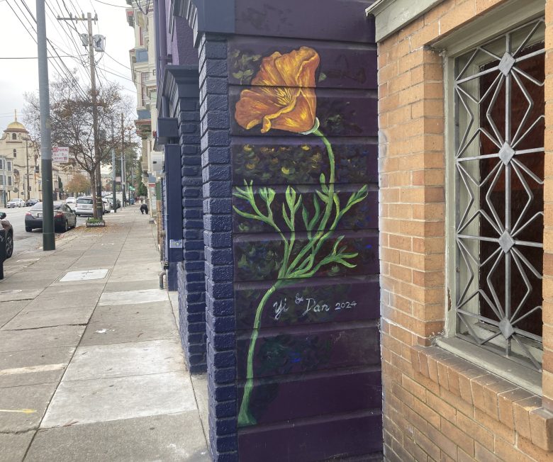 A mural of a California poppy with green stem and leaves is painted on a dark purple wall next to a sidewalk, signed "Dan 2022.