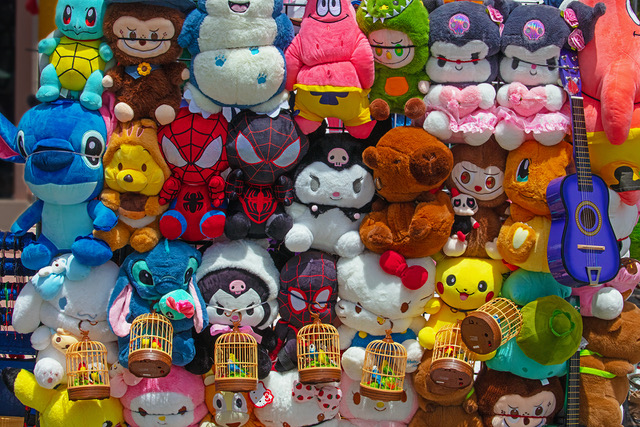 A display of various colorful stuffed animals and cartoon character plush toys, with several small birdcages hanging in front of them.