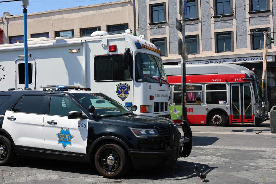 A San Francisco police SUV and mobile command vehicle are parked on a city street next to a red public transit bus.