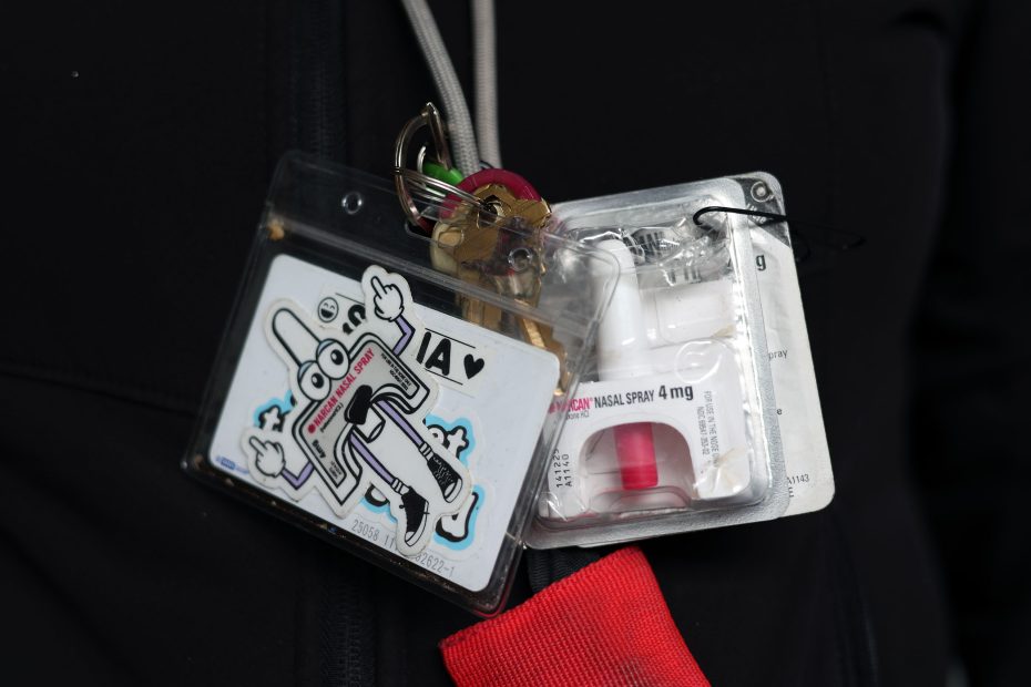 A set of keys, a cartoon-themed ID card, and a packaged nasal spray are attached to a lanyard worn around someone's neck.