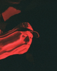 A distorted, red-tinted image shows a person wearing a baseball cap, with their face stretched horizontally in a wave-like effect.