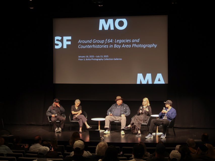 Five panelists sit on stage in front of an audience at SFMOMA, discussing "Around Group f.64: Legacies and Counterhistories in Bay Area Photography" with a presentation projected behind them.