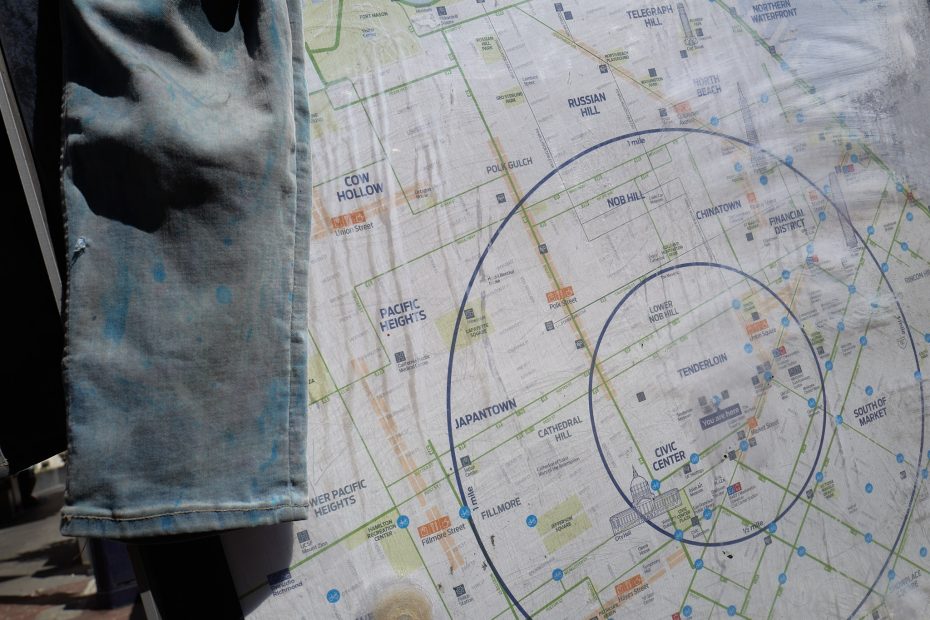 A close-up of a city map showing neighborhoods in San Francisco, with blue concentric circles drawn over it and a piece of fabric partially covering the left side.