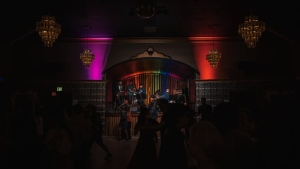 A band performs on a stage under colorful lights in a dimly lit venue, with people dancing in the foreground.