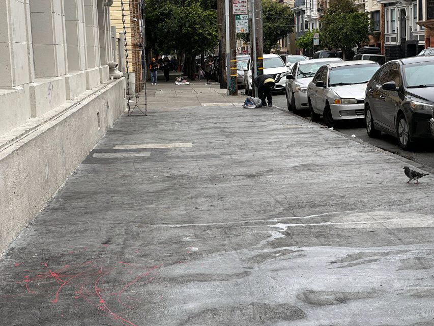A city sidewalk with scattered debris and a few pigeons, bordered by parked cars and buildings on a cloudy day.