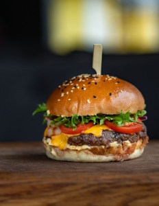 A cheeseburger with lettuce, tomato, cheese, and a beef patty on a sesame seed bun, held together with a wooden skewer, on a wooden surface.