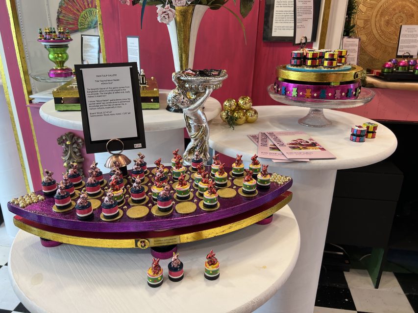 A display of colorful, decorative desserts on trays and cake stands in a vibrant, ornate setting with pink and gold accents.