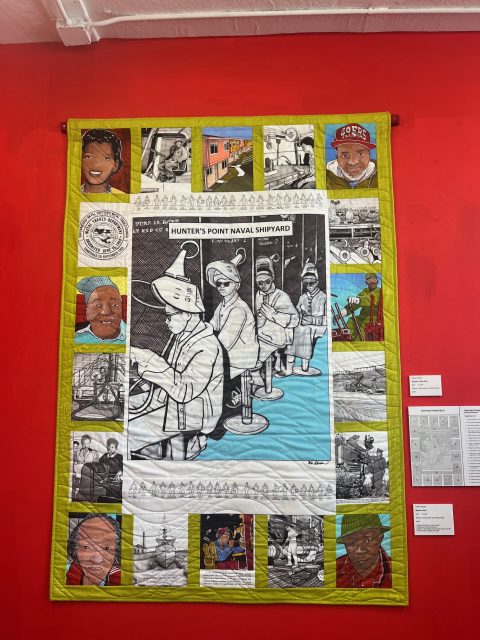 A quilt with a central black-and-white image of workers at the Hunter's Point Naval Shipyard, surrounded by colorful portraits and smaller scenes, displayed on a red wall.