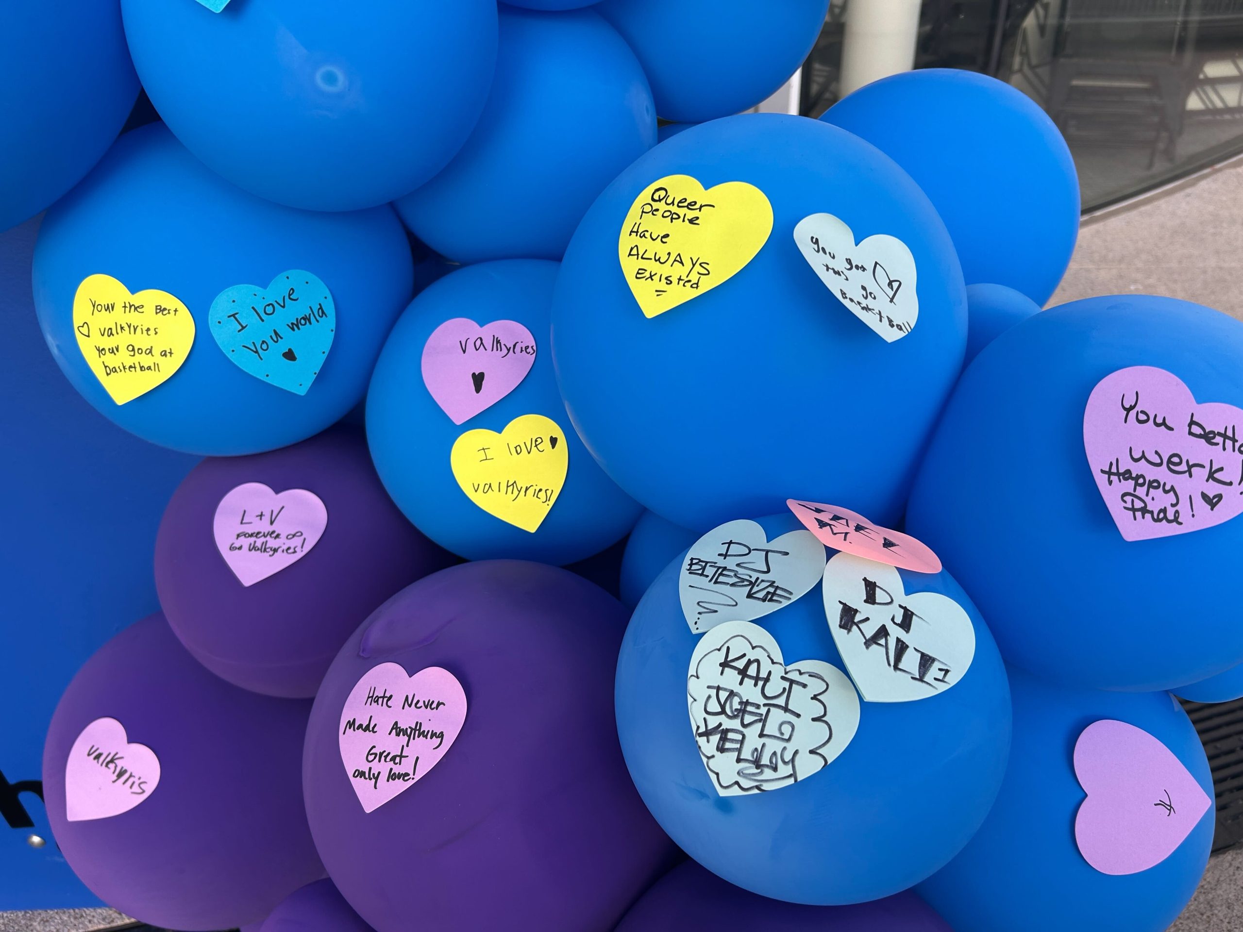 Cluster of blue and purple balloons decorated with colorful heart-shaped notes, each containing handwritten supportive and positive messages.