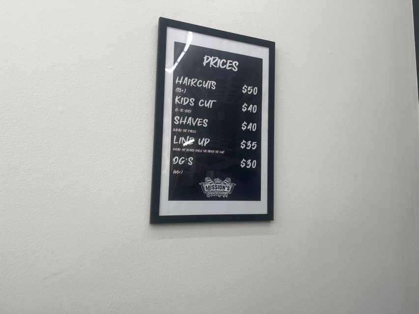 Framed price list on a white wall displaying various haircut and grooming services with prices ranging from $30 to $50.