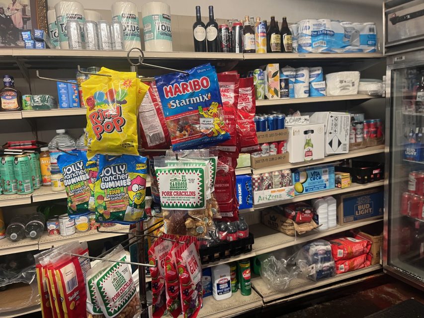 Shelves stocked with various drinks, snacks, and candy including Haribo Starmix, Jolly Rancher gummies, and Rip Pop, with a refrigerator and assorted beverages in the background.