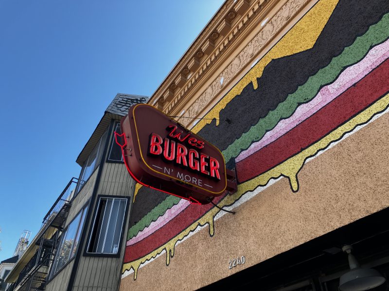A neon sign reading "Wes Burger N' More" is mounted on a wall painted with a large, colorful burger mural. The building number 2240 is visible below the sign.