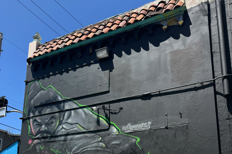 Mural of a hand holding a pool cue over a green table, with several colorful billiard balls scattered, painted on an exterior wall.