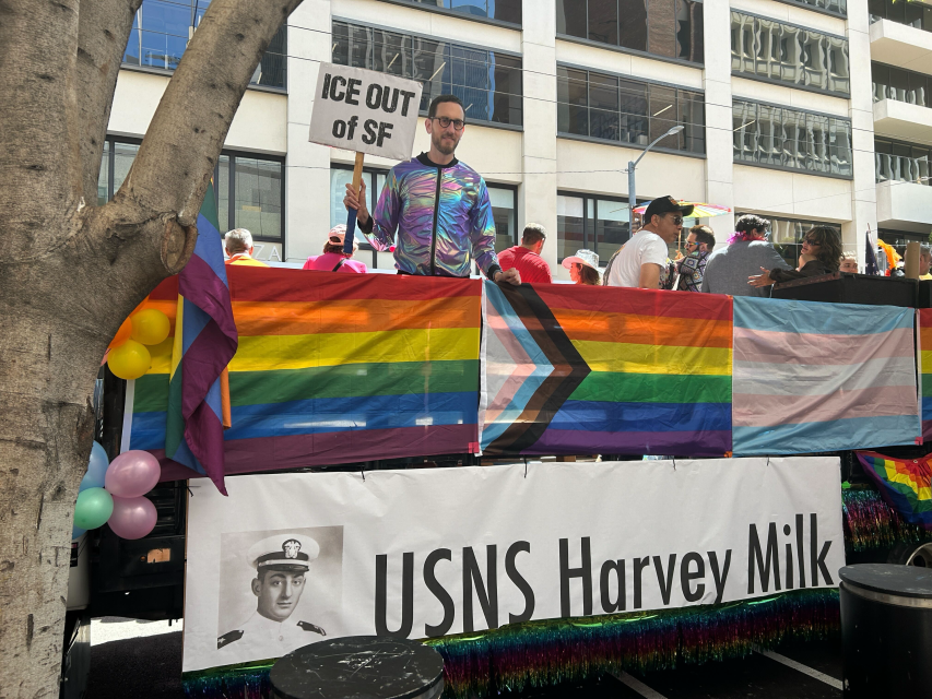 A person in a rainbow outfit holds a sign reading "ICE OUT of SF" on a float decorated with pride flags and a "USNS Harvey Milk" banner at a joyful parade.
