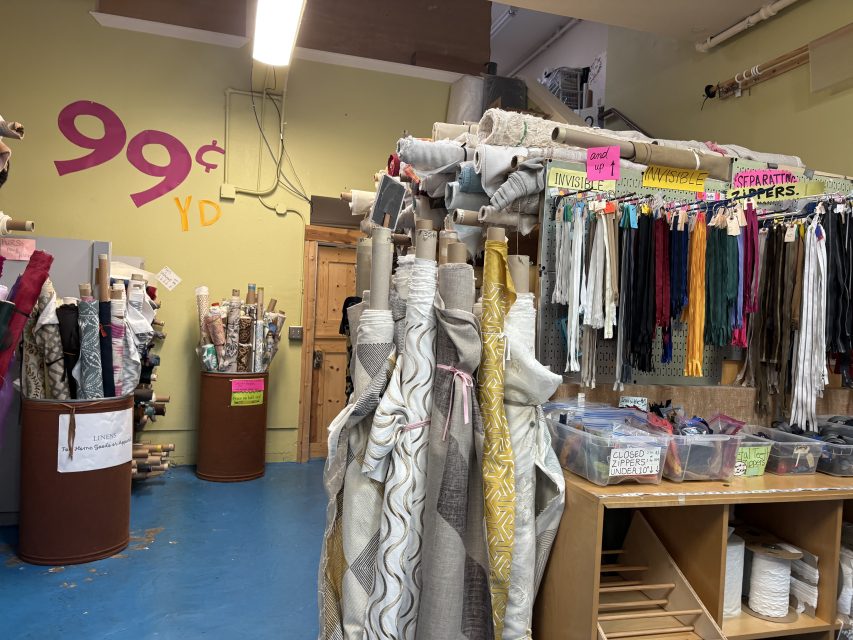 Fabric rolls, trims, and remnants are organized in bins and racks inside Fabrix, a fabric store with a "99¢ YD" sign displayed on the wall.
