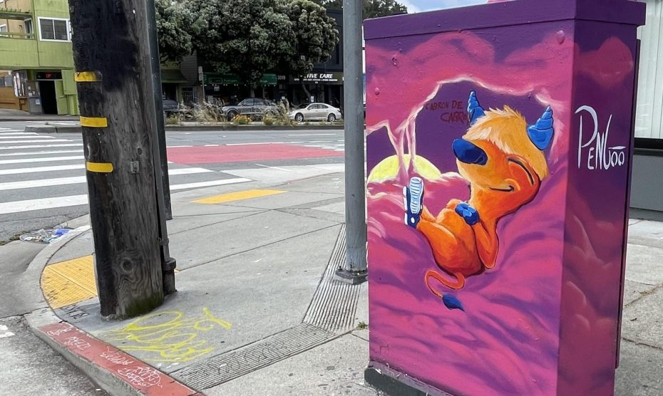 A painted utility box at a street corner features a cartoon creature lounging with a drink in hand, against a purple and pink background.