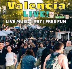 Crowd walking along a street lined with tents at an outdoor event. Text promotes "Valencia LIVE! Music, Art, Free Fun." Street signs and trees visible in the background.