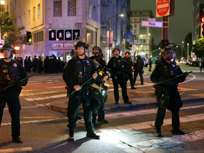 A group of police officers and ICE agents standing on a street.