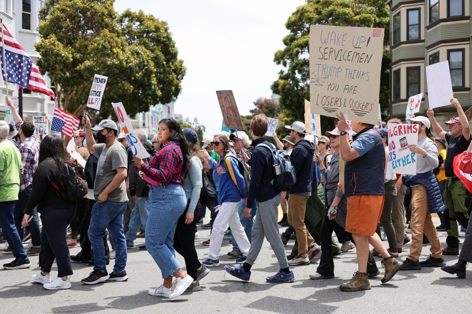 A group of people march down a city street holding flags and protest signs, joining together in a daytime demonstration for their cause.