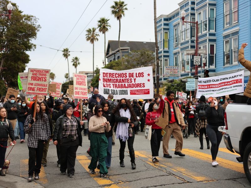 A diverse group of people march on a city street holding signs advocating for immigrant and workers' rights.